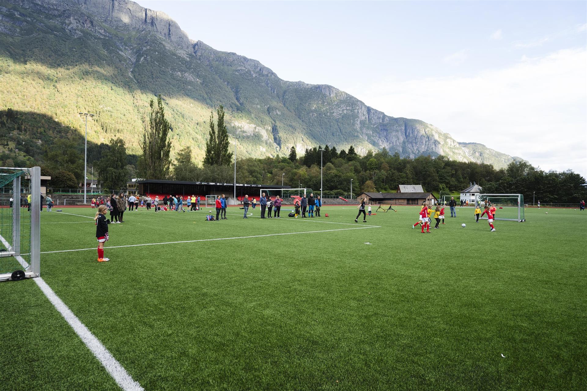 Barn som spiller fotballkamp på Eide kunstgressbane med fjell og himmel i bakgrunn. Foto.
