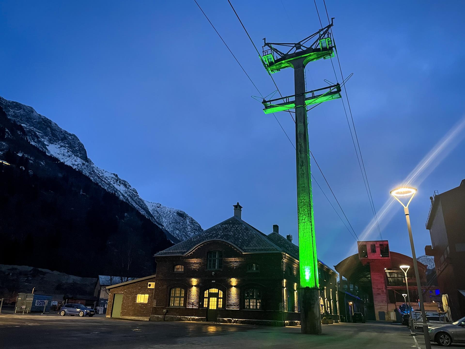Smelteverkstomta ein sein kveld med lyssetting av mast i grønt. Foto.