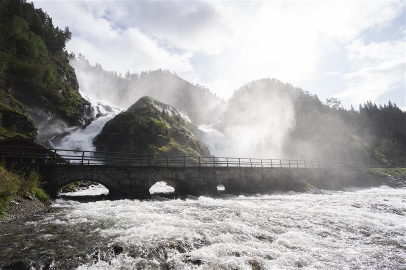 Foss som er delt i to av ein stor stein med ei gammal steinbru i framkant.