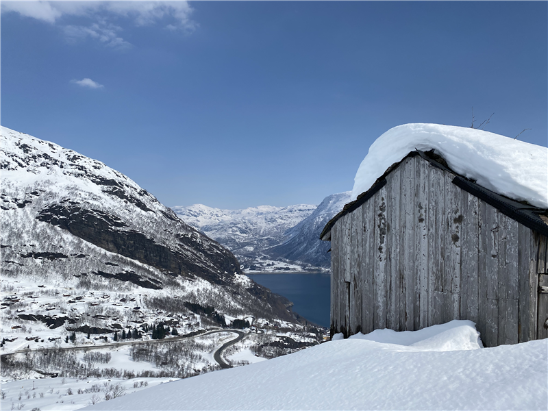 Gamal hytte i framgrunn med utsyn over Røldaslvatnet i snødekte omgivnadar. Bilete.