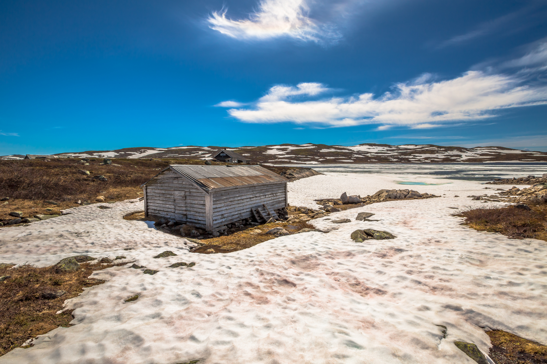 Gamalt naust i Hardangervidda nasjonalpark med snø, vatn og fjell