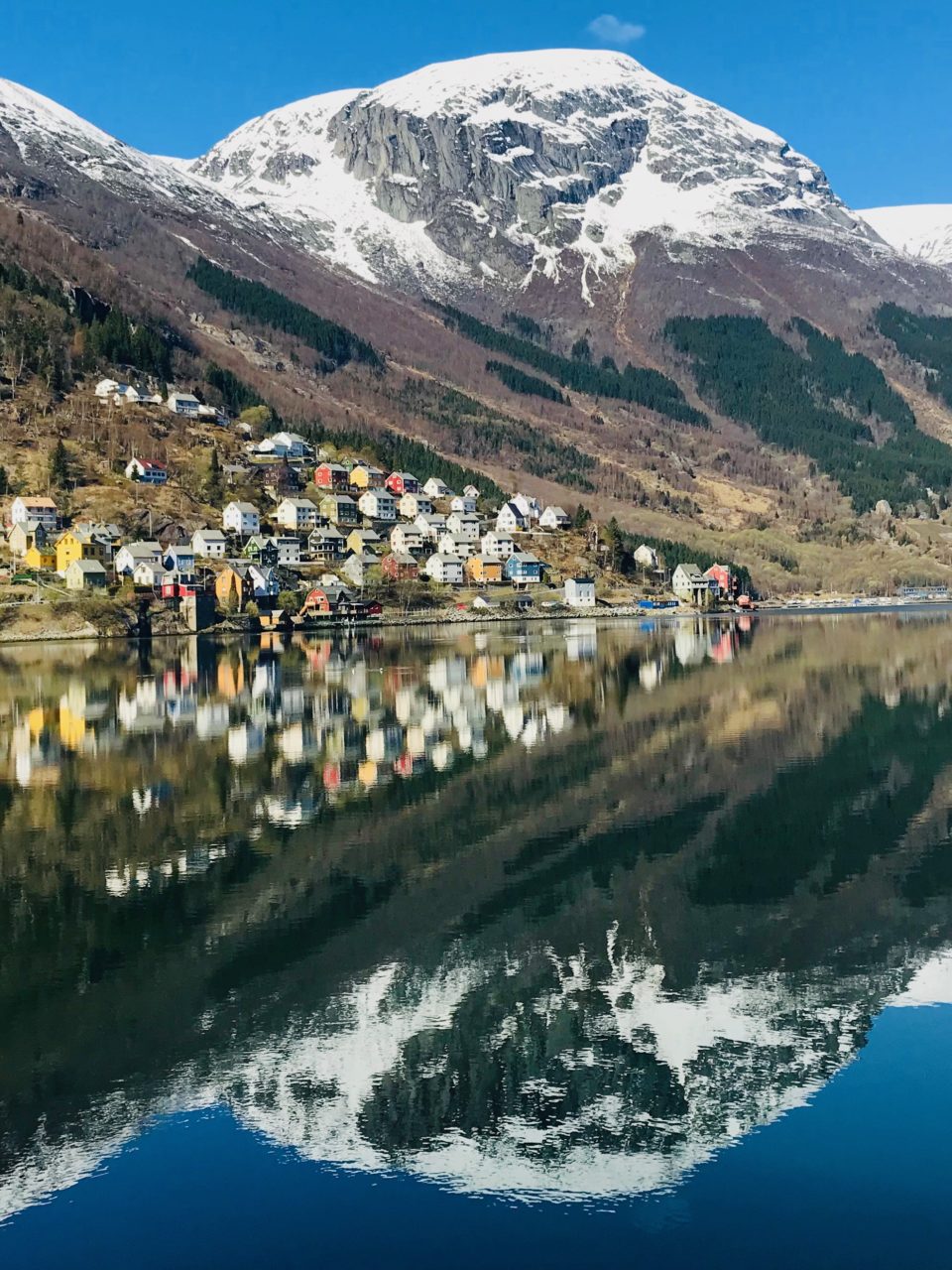 Utsyn over Kalvanes som speglar seg i fjorden i fint vær. Foto.