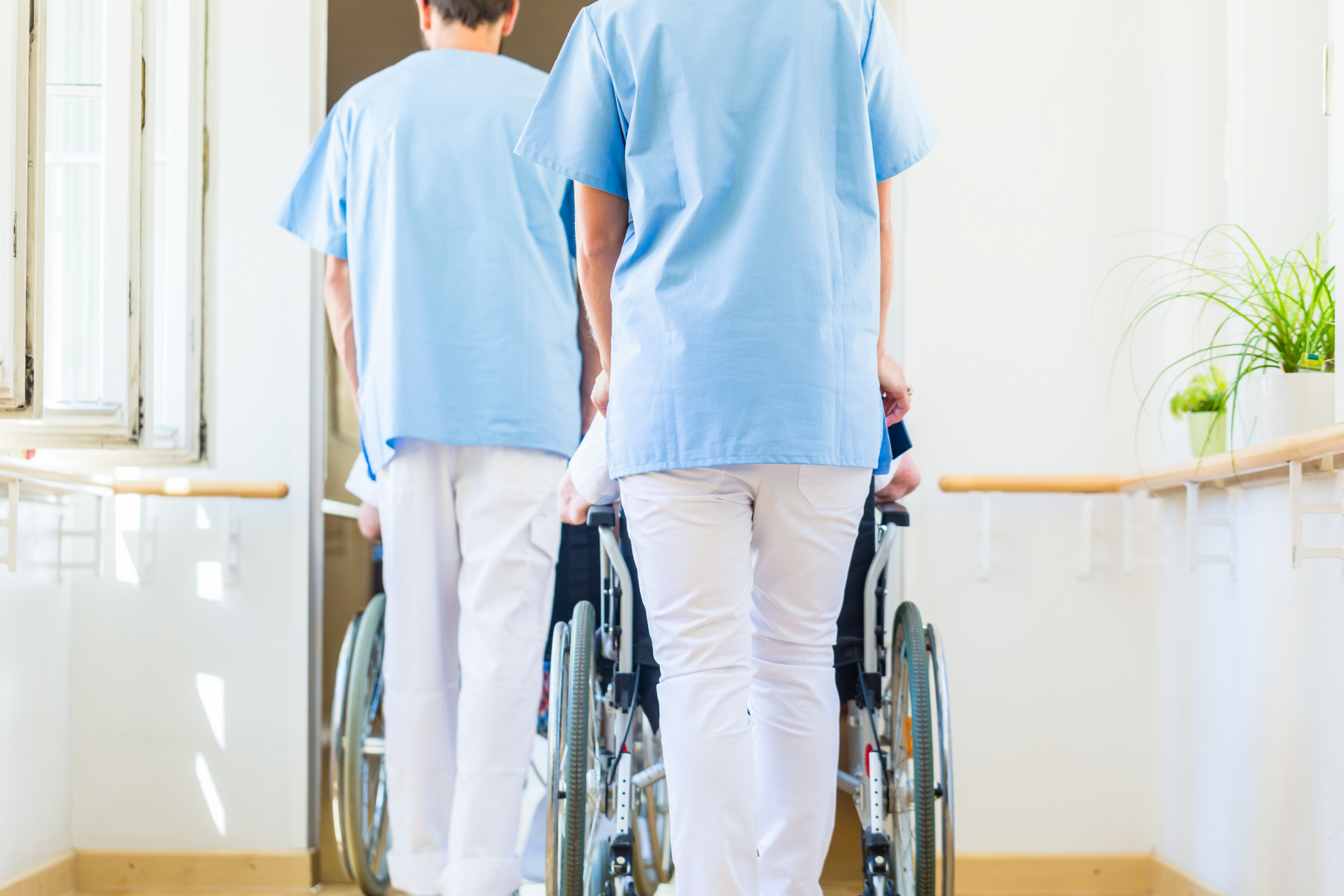 To sjukepleiarar triller pasienter i rullestol. Foto.