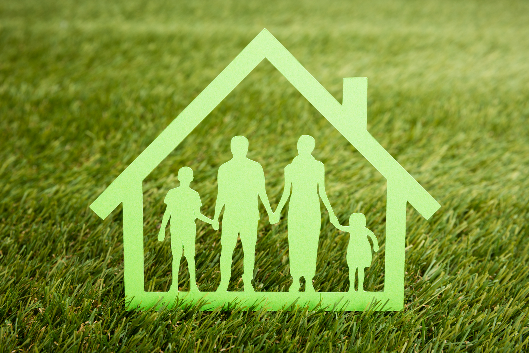 Grønt ikon av familie inne i eit hus med gras som bakgrunn.