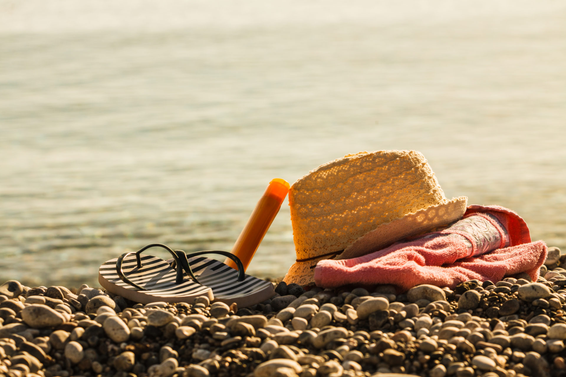 Sol hatt, flipp flopps, solkrem og dykkerbriller på steinettete strand. Bilete.