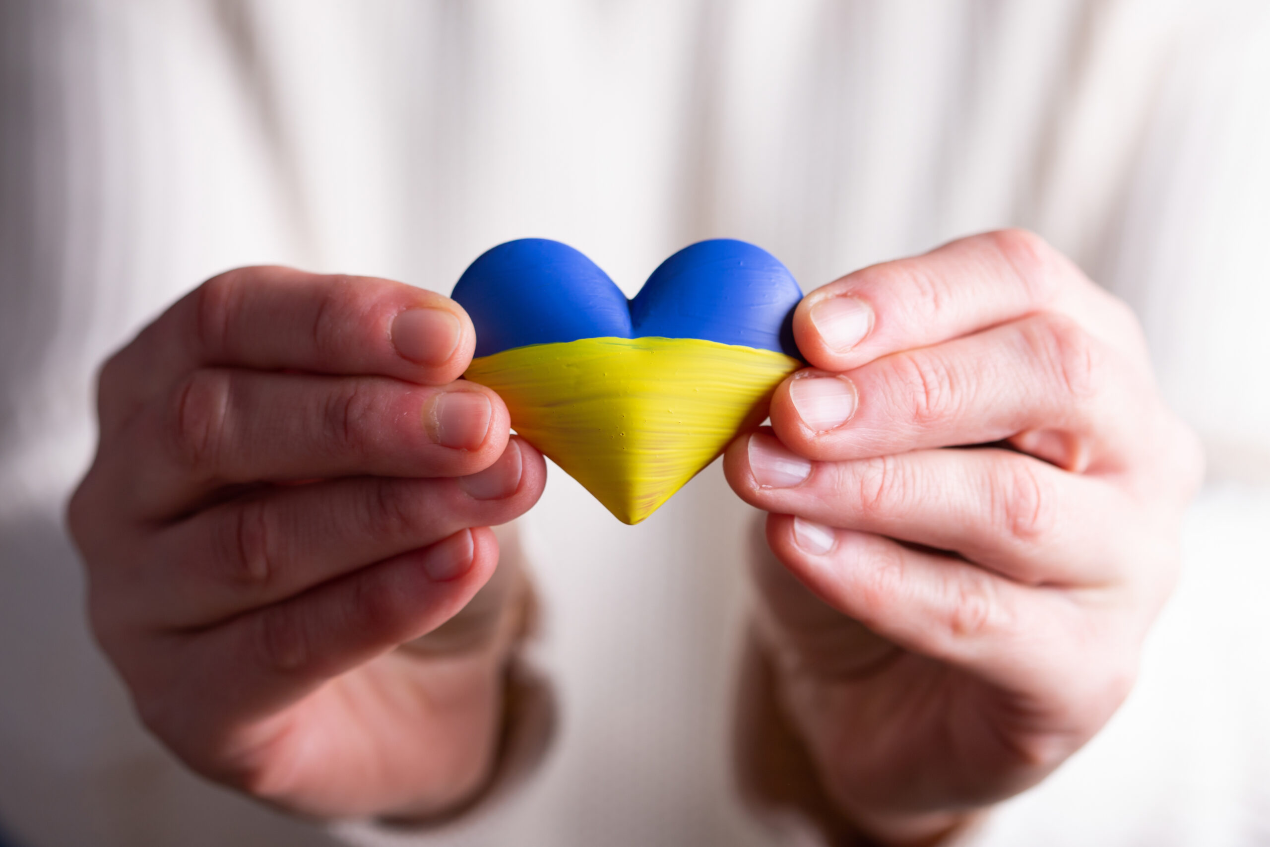 Ukrainske flagget forma som eit hjarta som vert halde fram av nokre hender for å symbolisera fred for Ukraina. Bilete.